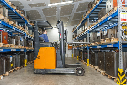 Warehouse worker driving forklift in storage for machine blocks