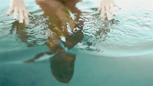 Beautiful naked girl reflection in the pure blue water. Gorgeous woman softly touches water surface and little fishes are swimming at her legs.  Young Nymph of lake Synevir in the Carpathians