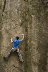 Athlete climbs on rock with rope.