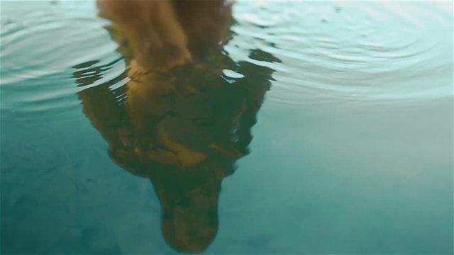 Young naked carpathian nymph plays with little fishes in the beautiful clean blue water of Synevir mountain lake. Reflection of naked woman body in the calm blue water close up. Slow motion shot
