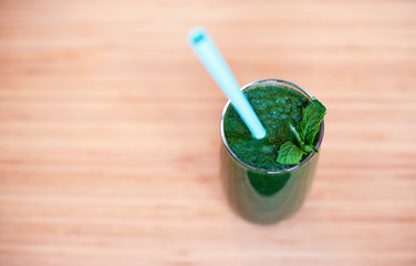 A glass of green smoothie with tube on wooden background