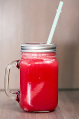 A watermelon smoothie in a mason jar with tube on wooden background