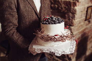 Wedding cake with berries in hands of groom. Rustic style of wedding. Modern decor of cake. 