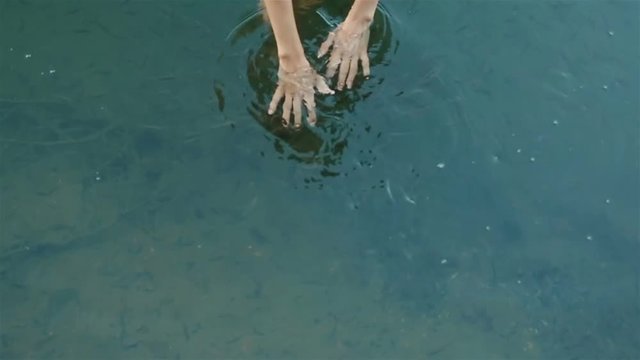 Reflection of beautiful fragile hands of fantasy young girl nymph in the cleah water with little healing fishes. Fish spa for skin care close up