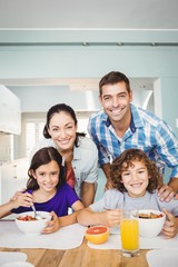 Portrait of cheerful man and woman with children having breakfast at home