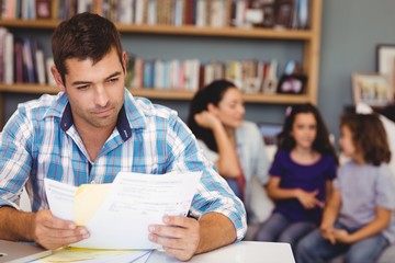 Close-up of man reading documents while family sitting in background at home