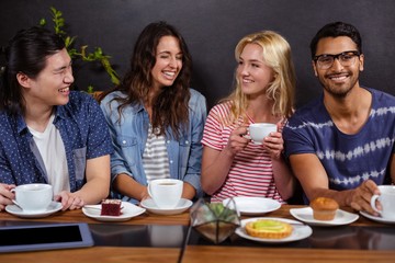 Smiling friends enjoying coffee together and using technologies