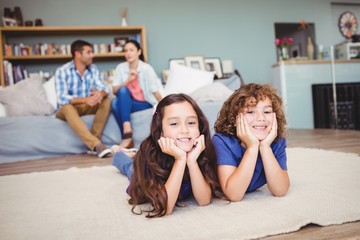 Portrait of children lying on carpet while parents sitting in background at home
