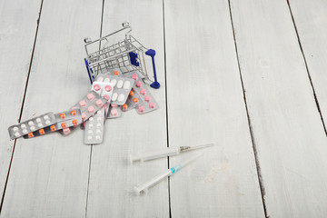 Shopping cart with pills and syringes on white wooden desk