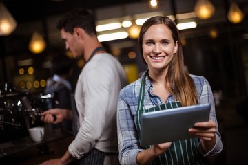 Pretty barista holding tablet and smiling at the camera