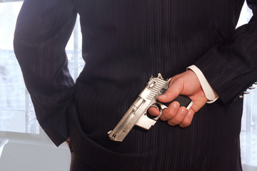 Mann im Anzug hält hinter dem Rücken eine Pistole 