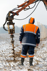 construction worker in uniform during holes boring in winter ground with drilling rig machine