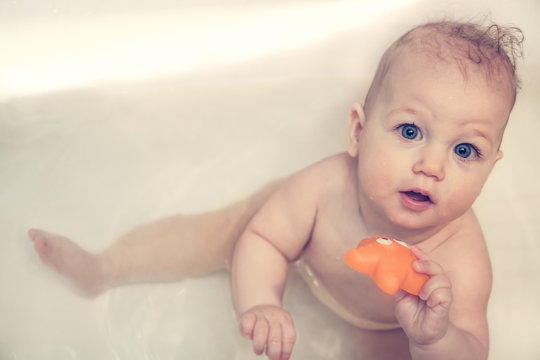 Cheerful baby looking up at camera while playing in bath