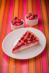 Raspberry tart and raspberries in ceramic jars on various colors background