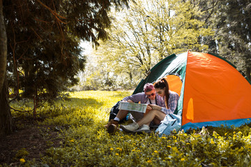Couple camping. Young couple sitting in front of the tent and examining the map.