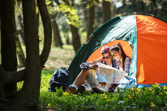 Couple camping. Young couple sitting in front of the tent and examining the map.