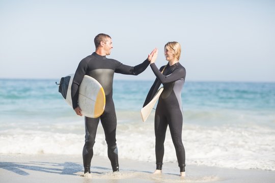 Couple holding a surfboard and giving a high five to each other on the beach