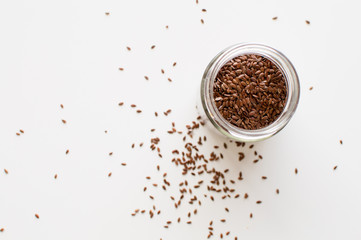 High angle view of flaxseed in glass jar and scattered on white table (selective focus)