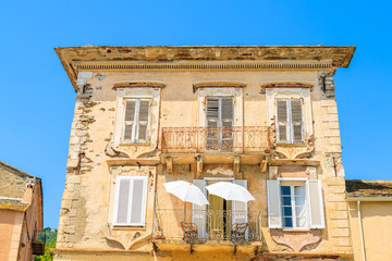 Two white sun umbrellas on balcony of a typical old house in Erbalunga town, Corsica island, France
