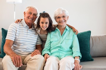 Portrait of grandmother and grand father with their granddaughter sitting on sofa in living room