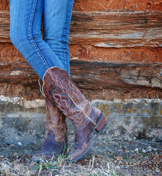 Western style image of cowgirl's legs in jeans and boots on deserted wall background