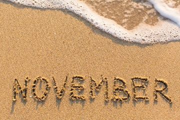 November - word drawn on the sand beach with the soft wave. Months series of 12 pictures.