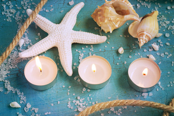 Fototapeta na wymiar Three burning candles, starfish and shells on the turquoise vint