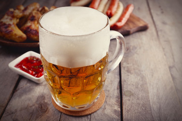 Glass of beer, chicken wings and grilled sausages on wooden table. Retro stylization