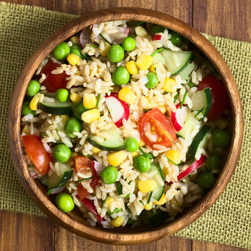 Brown Rice Salad With Cherry Tomato, Corn, Cucumber, Radish, Pea And Chives Served In Bowl, Photographed Overhead On Dark Wood With Natural Light (Selective Focus, Focus On The Top Of The Salad)