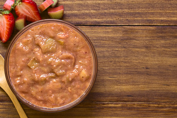 Homemade rhubarb and strawberry chutney in glass bowl, photographed overhead on dark wood with natural light