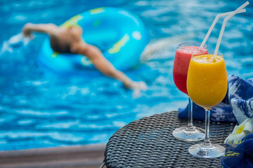 Two cocktails beside swimming pool. Woman in background