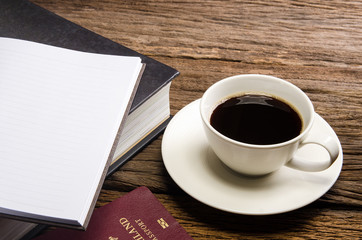 Cup off coffee on wooden deck tabletop with books and Thai passp