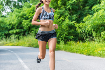 Fitness girl running in summer outdoor park. Happy fit athlete working out in sports bra and 2-in-1 compression shorts fashion activewear outfit showing off slim body and abs training for weight loss.