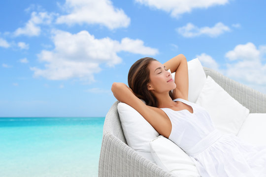 Sleeping woman relaxing lounging on white outdoor sofa day bed lounger on beach ocean background. Asian girl lying down laid back on pillows dreaming or enjoying the sun carefree happy. Home living.