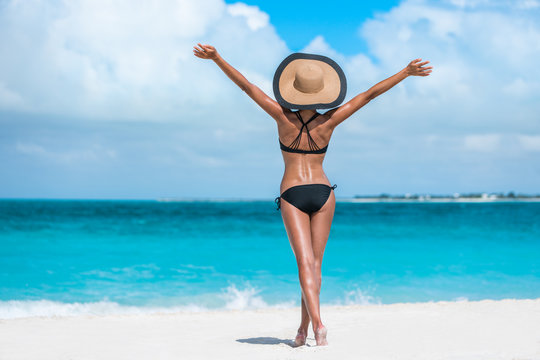 Summer vacation happiness carefree joyful sun hat woman with open arms in success enjoying body weight loss tropical beach destination. Holiday bikini girl relaxing from behind on Caribbean vacation. 