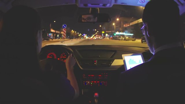 timelapse of businesswoman driving car in the city street and talking to her male colleague sitting on passenger seat and using digital tablet