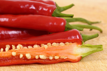 Group of several pile heap red chili or chilli peppers one cut sliced showing hot seeds inside on a wood cutting chopping board photo