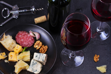 Glass and bottle of red wine, cheese, bread, garlic, nuts, salami on gray stone texture background. View from above