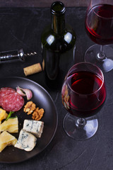 Glass and bottle of red wine, cheese, bread, garlic, nuts, salami on gray stone texture background. View from above