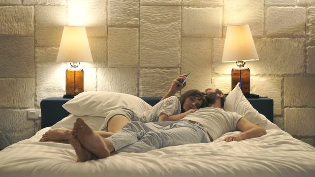 Couple in bed at night, man texting with lover on smartphone, wife sleeping 
