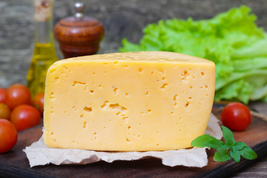 Tilsit Tilsiter cheese of the semi-hard cheese with vegetables on a wooden background