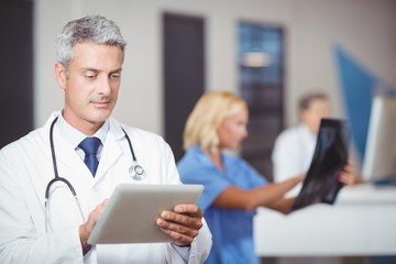 Male doctor using digital tablet with colleague checking X-ray