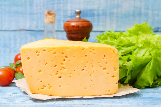 Tilsit Tilsiter cheese of the semi-hard cheese with vegetables on a wooden background