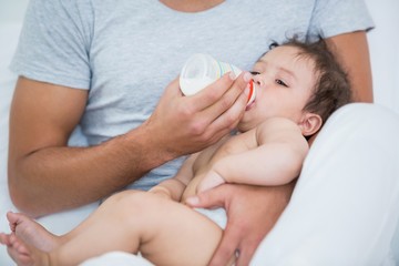 Obraz na płótnie Canvas Man feeding milk to baby girl at home