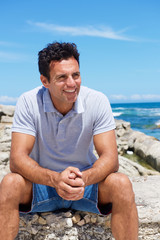 Smiling middle aged man sitting by the beach