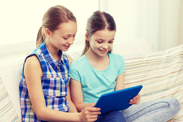 happy girls with tablet pc sitting on sofa at home