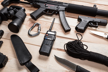 Assault rifle, gun, knife with sheath, compass and notebook with pen on table.