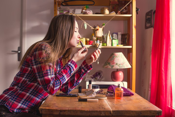 Young woman doing her makeup at the table at home and paints her lips with lipstick