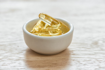 Cod liver oil omega 3 gel capsules in bowl on floor wood
