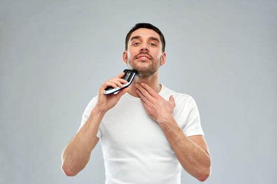 smiling man shaving beard with trimmer over gray